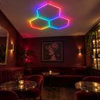 Mise en situation illustrative du kit Plafonnier LED Hexagonal RGB Nid d'Abeille 3 Modules Hexeli™ 1,68 m x 1,66 m – RGB connecté, ambiance RGB lounge. Création commerciale, pas une photo de client réel.
